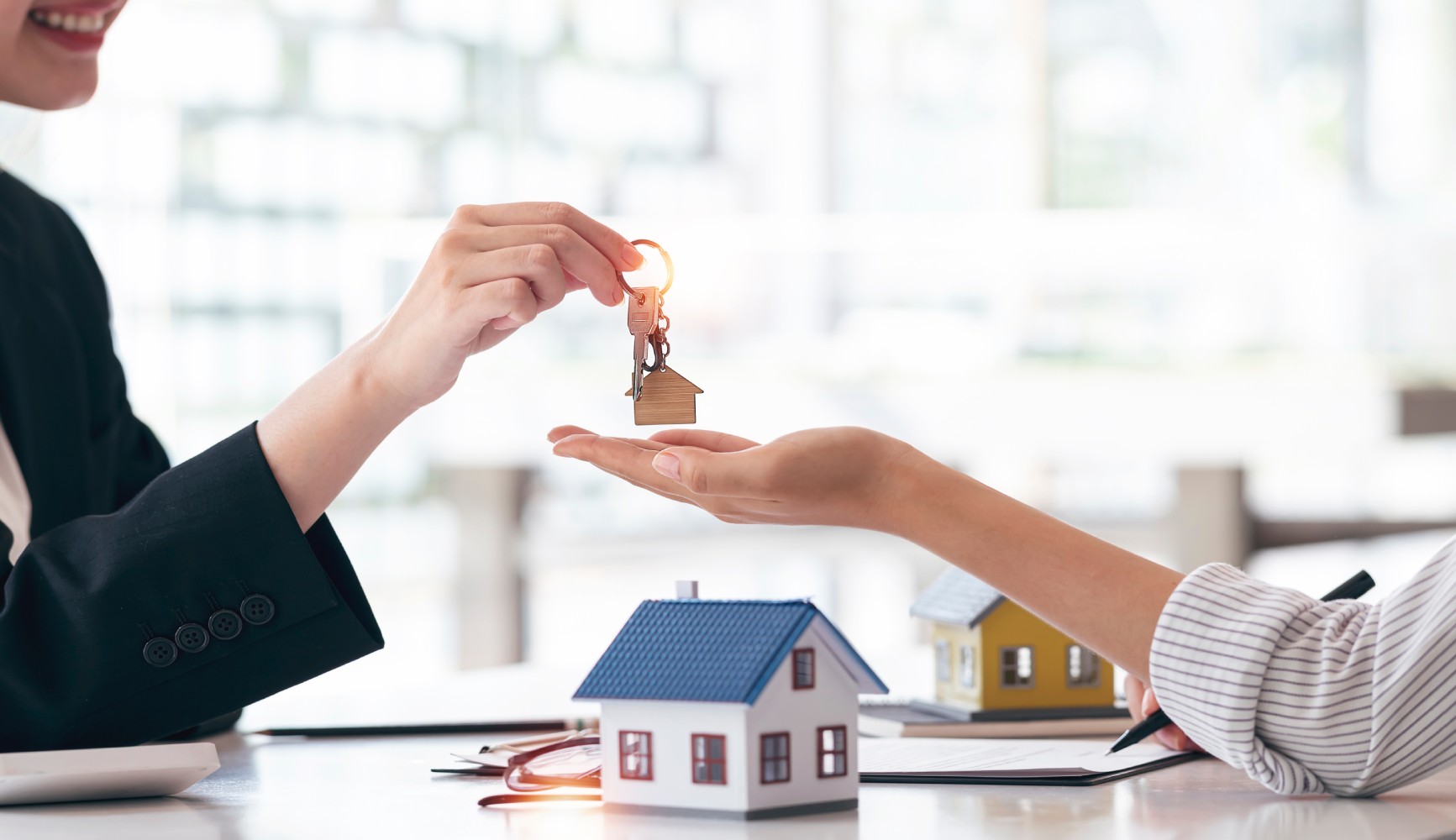 A realtor hands over house keychains to a homebuyer in an office, symbolizing a successful property sale.
